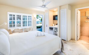 Ein Schlafzimmer mit einem Bett, einem Schreibtisch und einem Stuhl. Es gibt ein Fenster mit Jalousien, einen Deckenventilator und eine Tür zu einem Badezimmer.