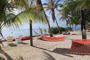 Ein Strand mit weißen Stühlen, einer roten Hängematte und einem roten Liegestuhl.