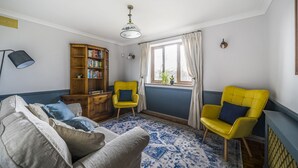Ein Wohnzimmer mit einer Couch, zwei gelben Sessel, einem Bücherregal aus Holz und einem Fenster mit Vorhängen.