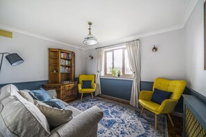 Ein Wohnzimmer mit einer Couch, zwei gelben Sessel, einem Bücherregal aus Holz und einem Fenster mit Vorhängen.