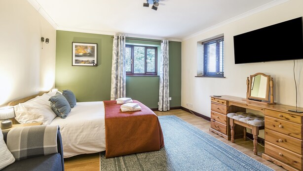 Ein Schlafzimmer mit Bett, Kommode, Fernseher und einem Fenster mit Vorhängen.