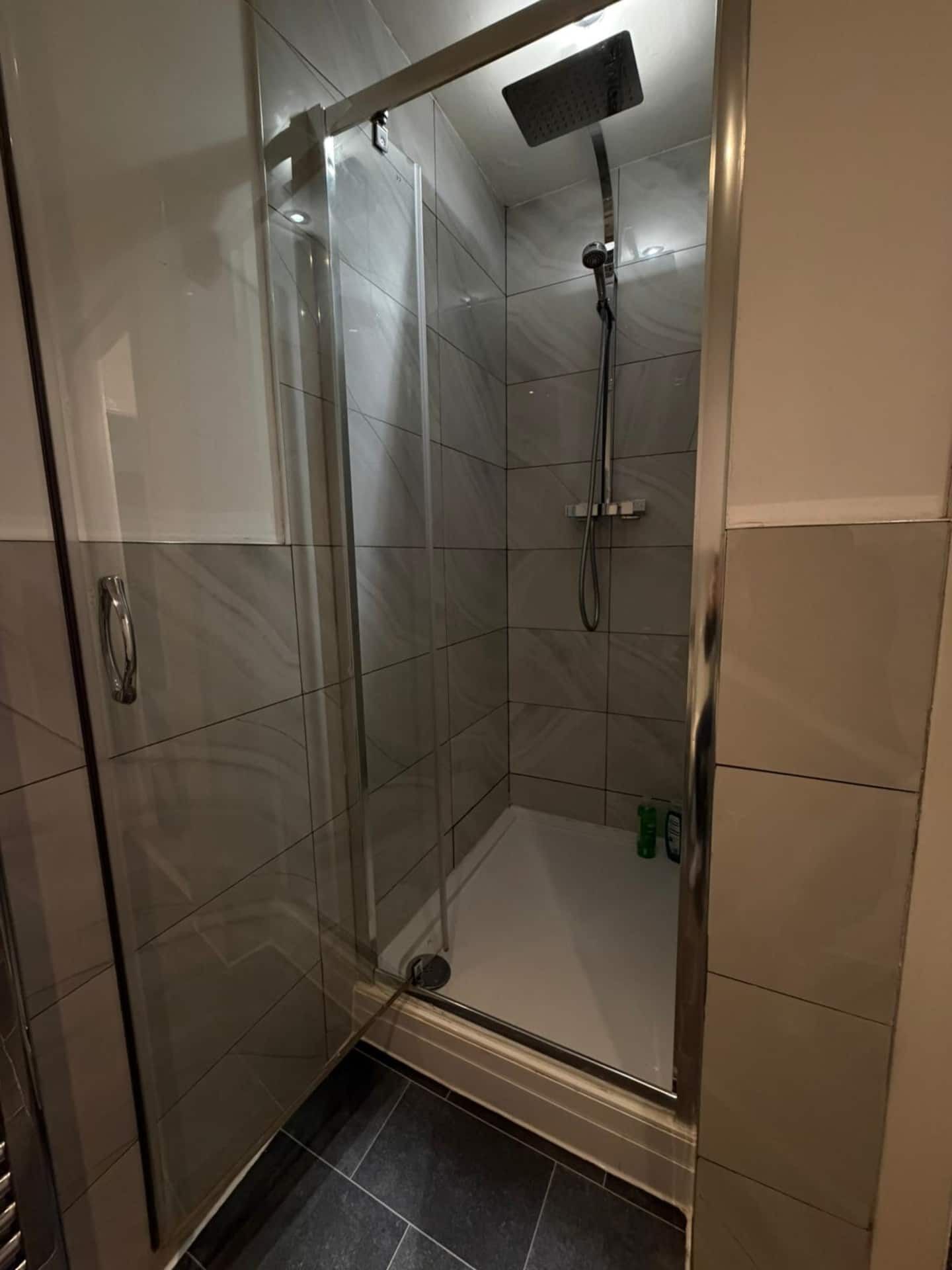 A glass-enclosed shower stall with a handheld showerhead and a handheld shower head on the wall.