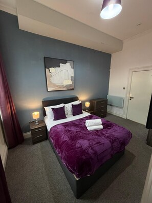A bedroom with a bed, nightstands, a dresser, a door, and a painting on the wall. - Spacious 4BR City Apartment | Terrace + Sleeps 10 (Liverpool)