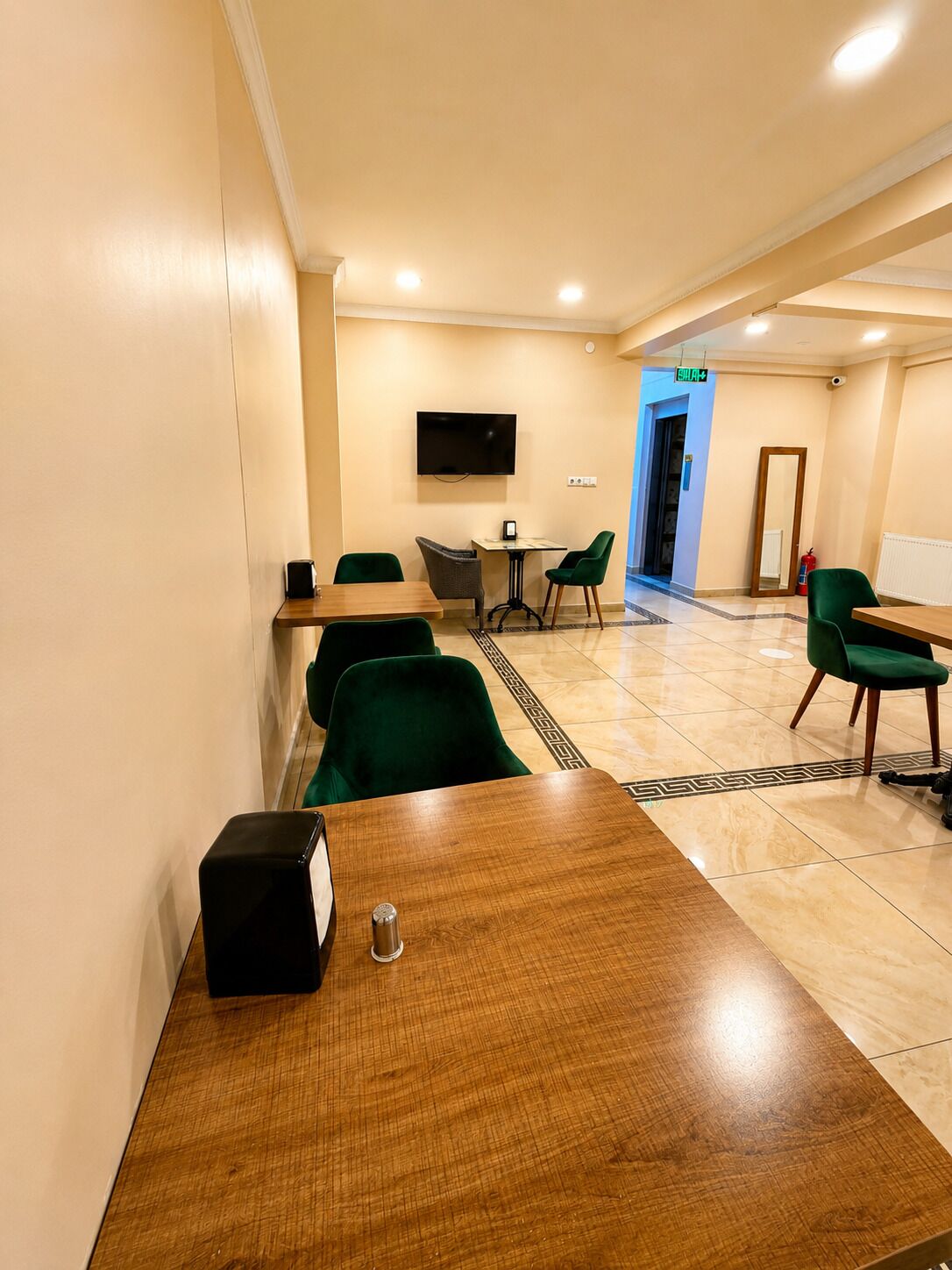 Ein Hotelzimmer mit einem Holztisch, grünen Stühlen, einem Flachbildfernseher und einer Tür zu einem Flur.