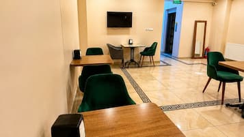 Habitación de hotel con una mesa de madera, sillas verdes, un televisor de pantalla plana y una puerta que da a un pasillo.