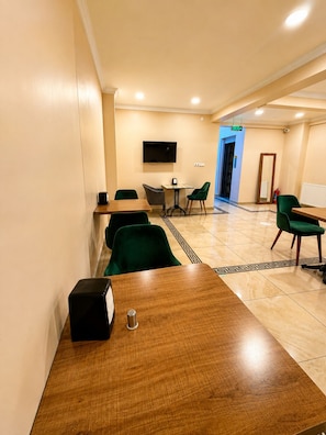 Habitación de hotel con una mesa de madera, sillas verdes, un televisor de pantalla plana y una puerta que da a un pasillo.