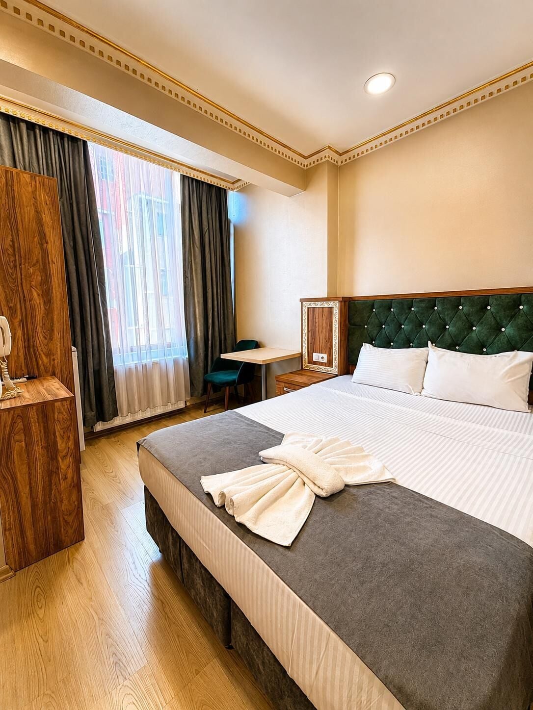 A hotel room with a large bed, a desk, a chair, and a wardrobe.