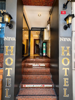 Entrada de un hotel con una escalera que conduce al interior, un mostrador de recepción y un letrero que indica la habitación número 21.