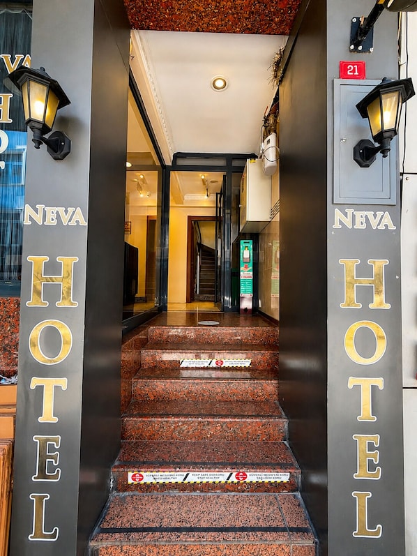 A hotel entrance with a staircase leading to the interior, a reception desk, and a sign indicating room number 21. - NEVA HOTEL (Istanbul)