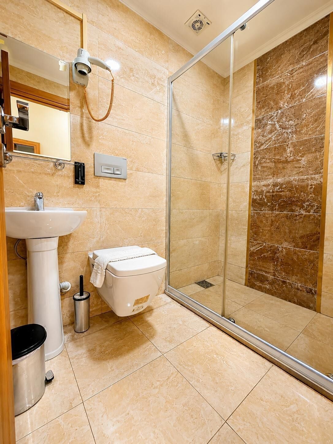 Un baño moderno con ducha envuelta en vidrio, lavabo sobre pedestal y retrete.