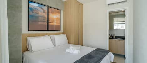 Una habitación de hotel moderna con una cama bien hecha, un cuadro de un atardecer y vistas al área de la cocina.
