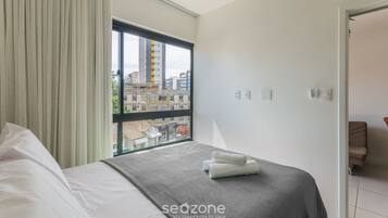 Una camera d'albergo con un letto, una finestra con tende, vista su edifici e una porta che conduce a un'altra stanza.