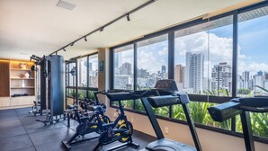 Una palestra con attrezzature per esercizi, ampie finestre e vista sulla città.