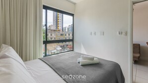 Una camera d'albergo con un letto, una finestra con tende, vista su edifici e una porta che conduce a un'altra stanza.
