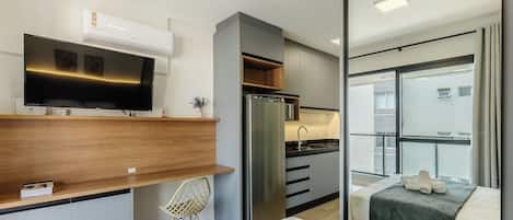 A compact hotel room with a kitchenette, a flat-screen TV, a bed with a view, and a small seating area.