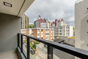 Ein Balkon mit Blick auf eine Stadtlandschaft, darunter mehrstöckige Gebäude und parkende Autos.