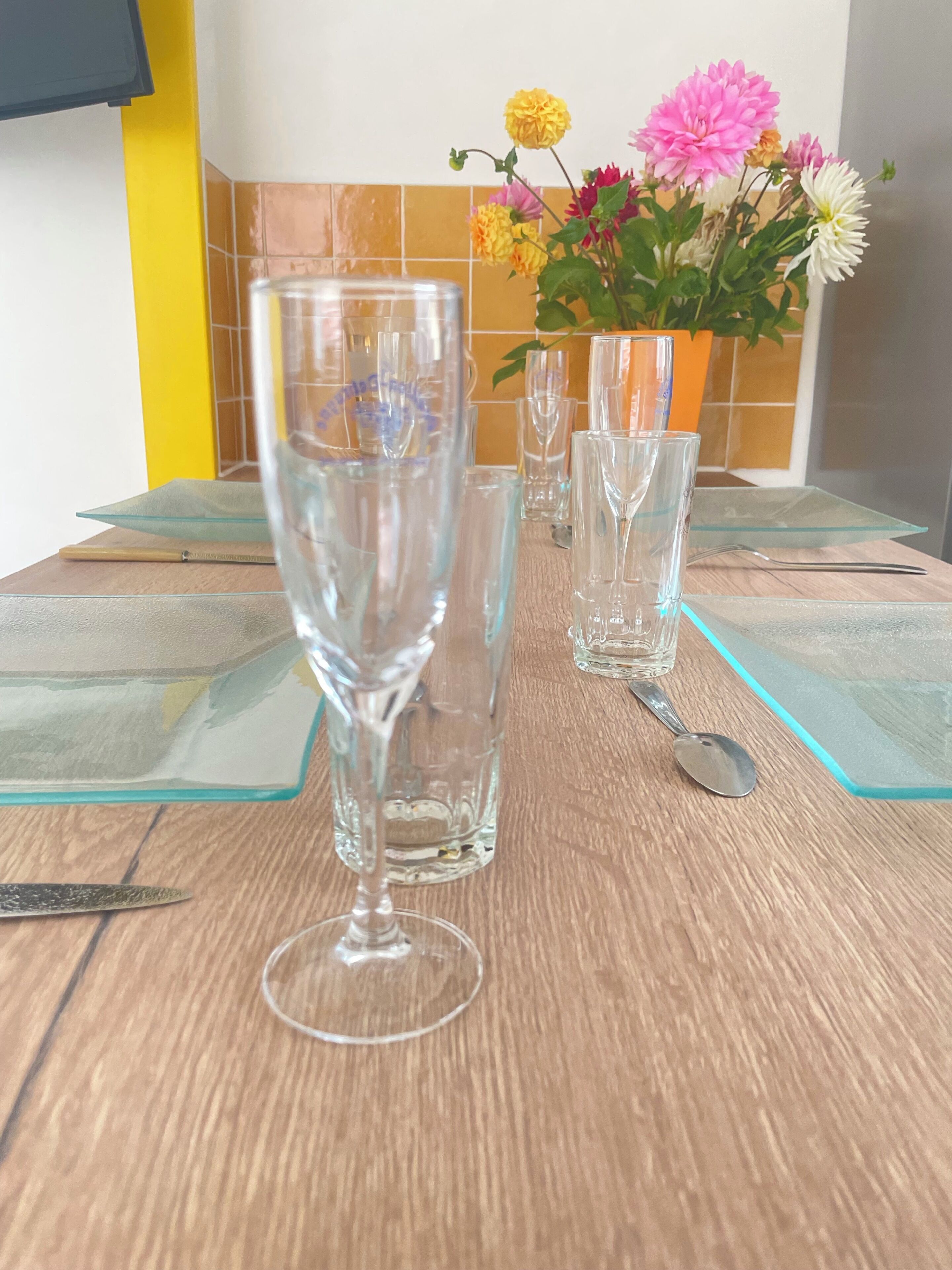 A table with clear glassware and a spoon, a potted plant with flowers, and a tiled backsplash.