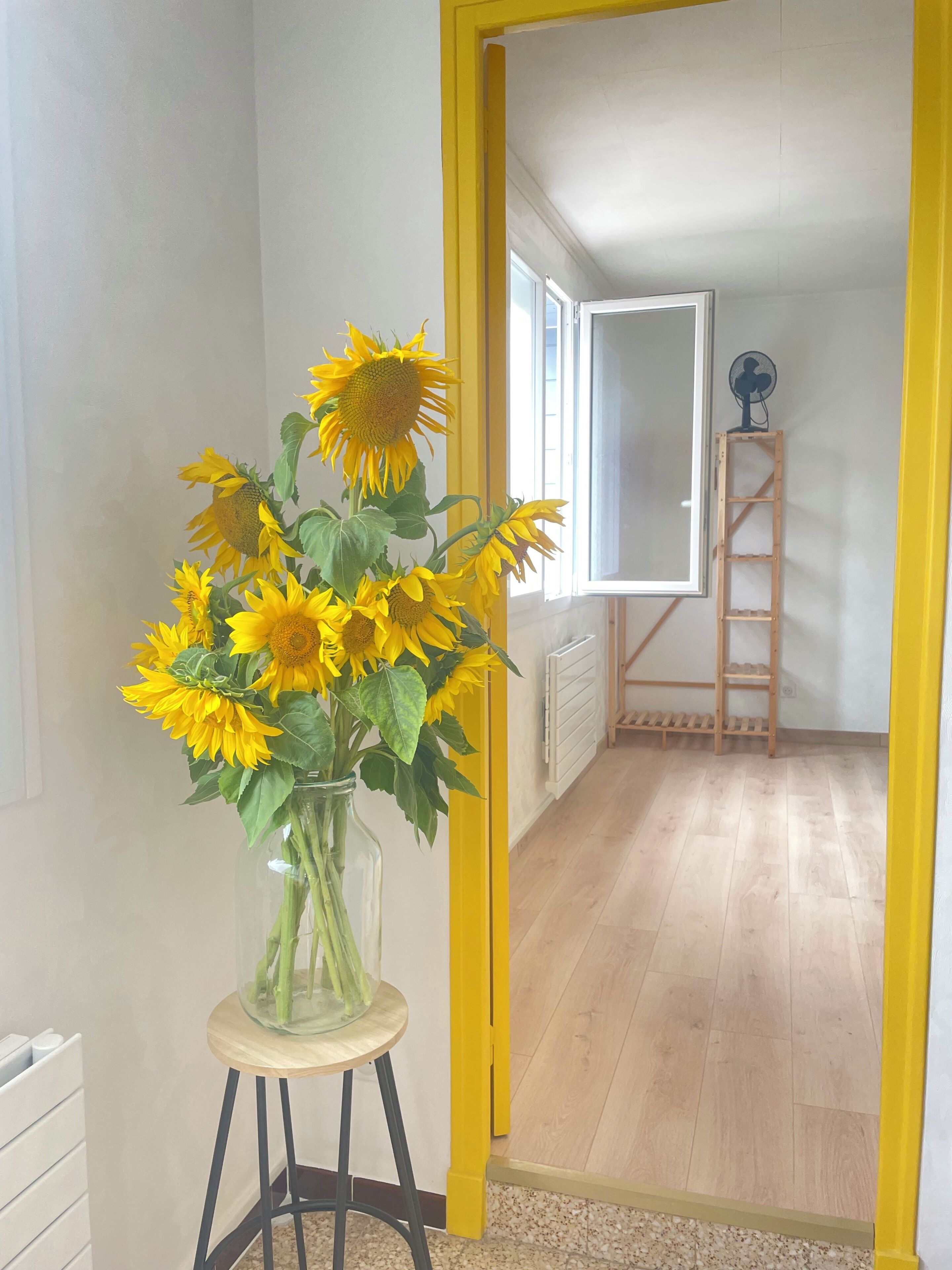 A room with a wooden floor, a yellow door frame, and a window with blinds.