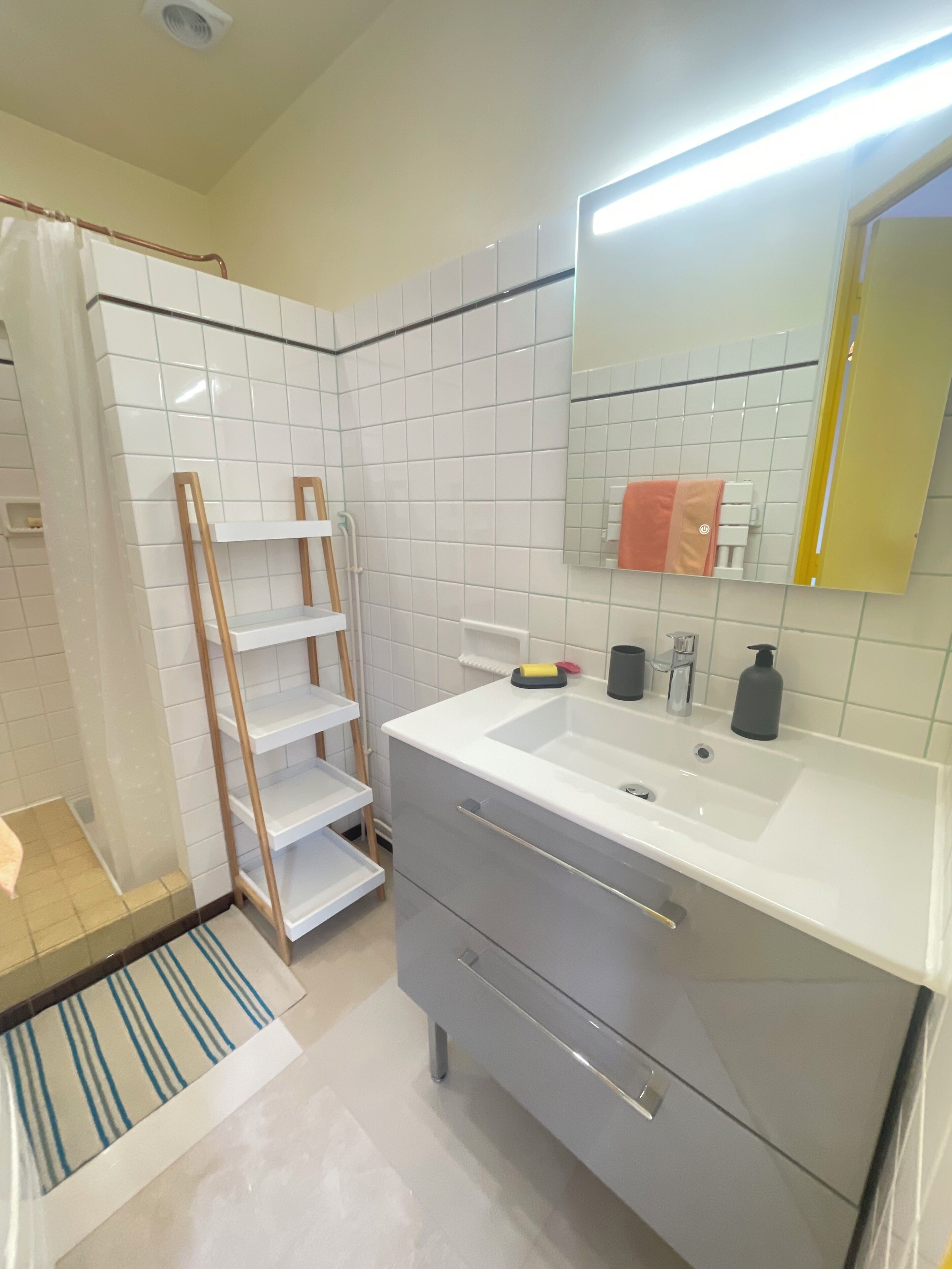 Une salle de bain moderne avec des carreaux blancs, un lavabo blanc, un miroir et un porte-serviettes.