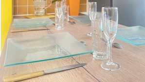 A kitchen with a clock, a refrigerator, a table set with glasses and a knife, and a vase of flowers.