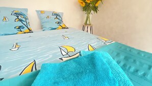 A bed with a blue and yellow sailboat pattern, a blue towel, and a vase with sunflowers.