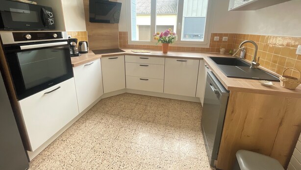 A kitchen with white cabinets, a black oven, a microwave, a sink, and a window with a view of the outside.