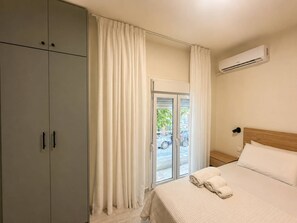 A hotel room with a bed, a wardrobe, a window with curtains, an air conditioning unit, and a view of the outside. - Sage & Oak Boutique Studio near City Center (Thessaloniki)