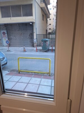 Blick durch ein Fenster auf eine Straße mit einer geschlossenen Garagentür, einem geparkten Auto und einer gelben Absperrung.
