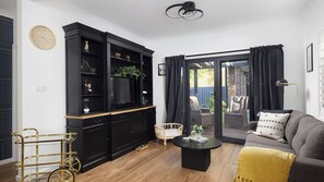 A living room with a black entertainment unit, a sofa, a coffee table, and a wicker chair. - Sandy Toes – Three Lux Retreats with Heated Pool (Nelson Bay)