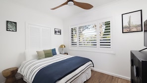 A bedroom with a bed, a ceiling fan, a window with shutters, and framed pictures on the wall. - Sandy Toes – Three Lux Retreats with Heated Pool (Nelson Bay)