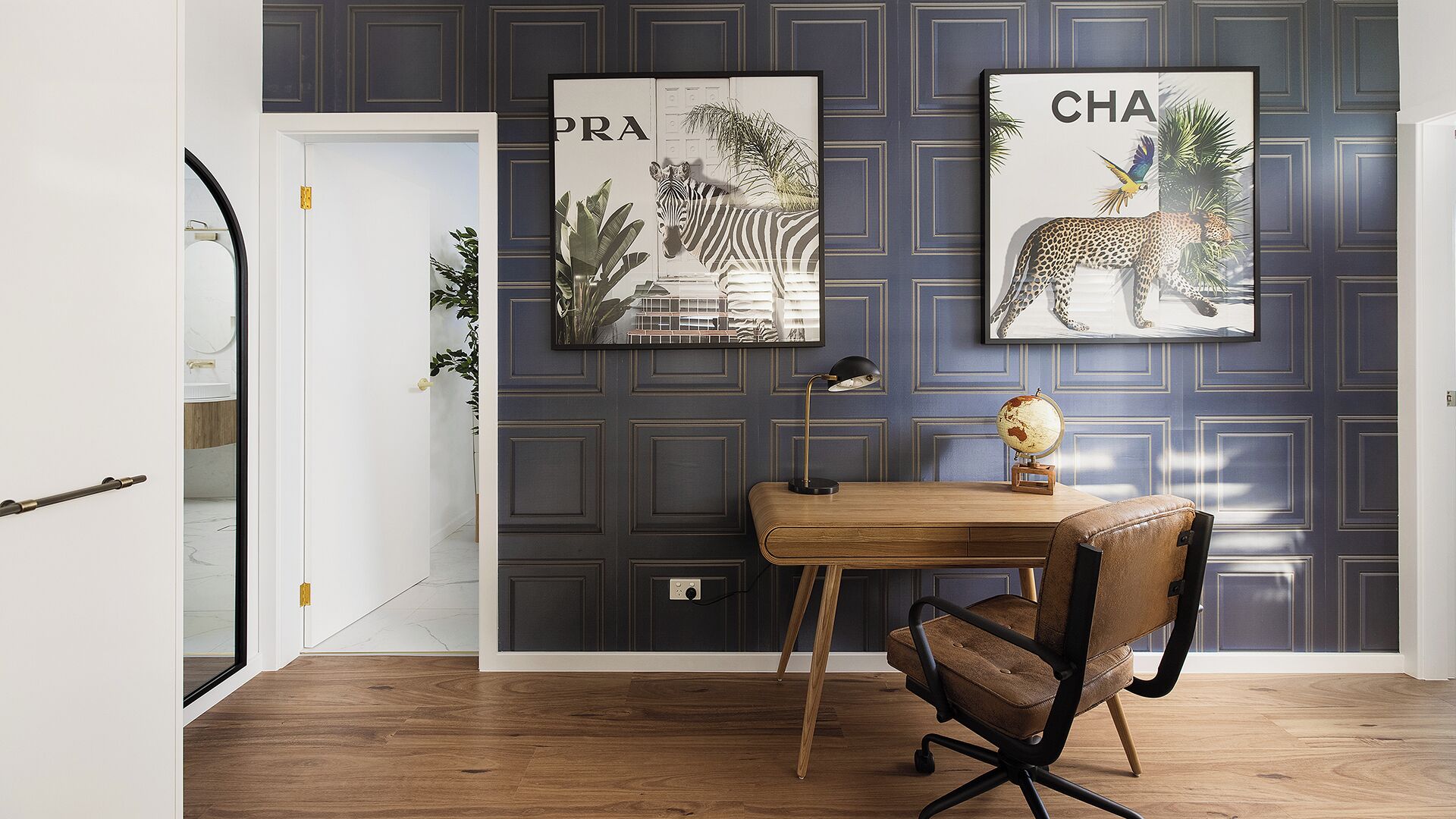 A room with a desk, chair, and two framed artworks on the wall.