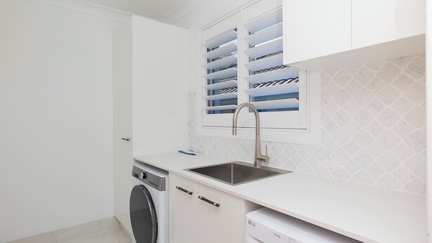 A compact kitchen with a built-in washing machine, a stainless steel sink, and white cabinetry. - Sandy Toes – Lux Retreat with Heated Pool (Nelson Bay)