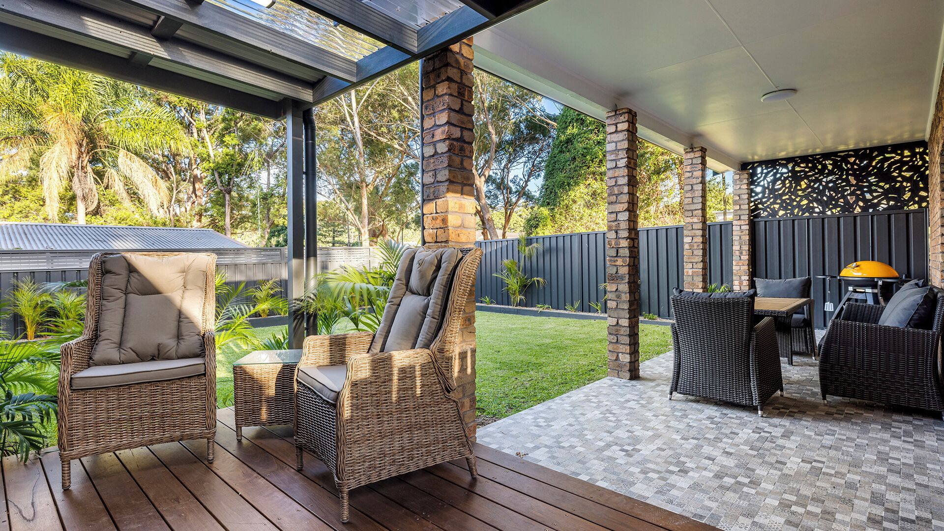 Un espace extérieur aménagé en terrasse, avec des meubles en osier, un barbecue et une vue sur le jardin.