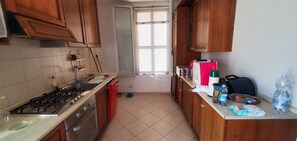 A kitchen with a gas stove, oven, and a sink. There are cabinets, a window with blinds, and various items on the counter. - Peaceful 3-bedroom country house in charming Trinità awaits you (Trinità)