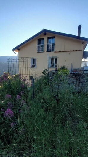 A two-story house with a sloped roof, a stone wall, and a metal fence. - Peaceful 3-bedroom country house in charming Trinità awaits you (Trinità)
