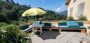 An outdoor seating area with a table and chairs, a yellow umbrella, and a view of a mountainous landscape. - Peaceful 3-bedroom country house in charming Trinità awaits you (Trinità)