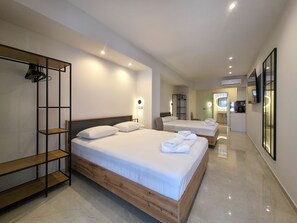 A modern hotel room with two beds, a wooden headboard, a built-in wardrobe, and a bathroom visible through an open door. - Odyssey Superior Junior Suite (Paralia)