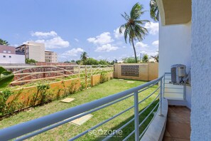 Un balcón con vista a una zona verde, una palmera y un edificio al fondo.