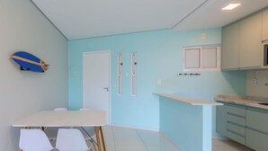Uma cozinha moderna com paredes azul claras, armários brancos, bancada branca e uma área de jantar com mesa e cadeiras.