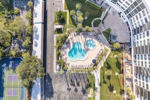 An aerial view of a resort with a central pool area, lounge chairs, and a tennis court. - 2BD Condo with Pool and Patio Ground Floor (Siesta Key)
