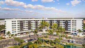 A multi-story hotel with a parking lot, palm trees, and a swimming pool. - 2BD Condo with Pool and Patio Ground Floor (Siesta Key)