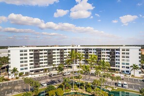A multi-story hotel with a parking lot, palm trees, and a swimming pool. - 2BD Condo with Pool and Patio Ground Floor (Siesta Key)