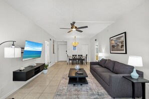 A modern living room with a flat-screen TV, a ceiling fan, a dining area with chairs and a table, and a gray sofa. - 2BD Condo with Pool and Patio Ground Floor (Siesta Key)