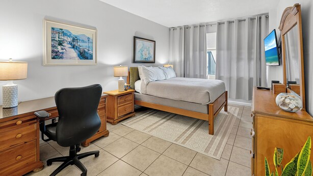 A hotel room with a bed, a desk with a chair, a TV, and artwork on the walls. - 2BD Condo with Pool and Patio Ground Floor (Siesta Key)