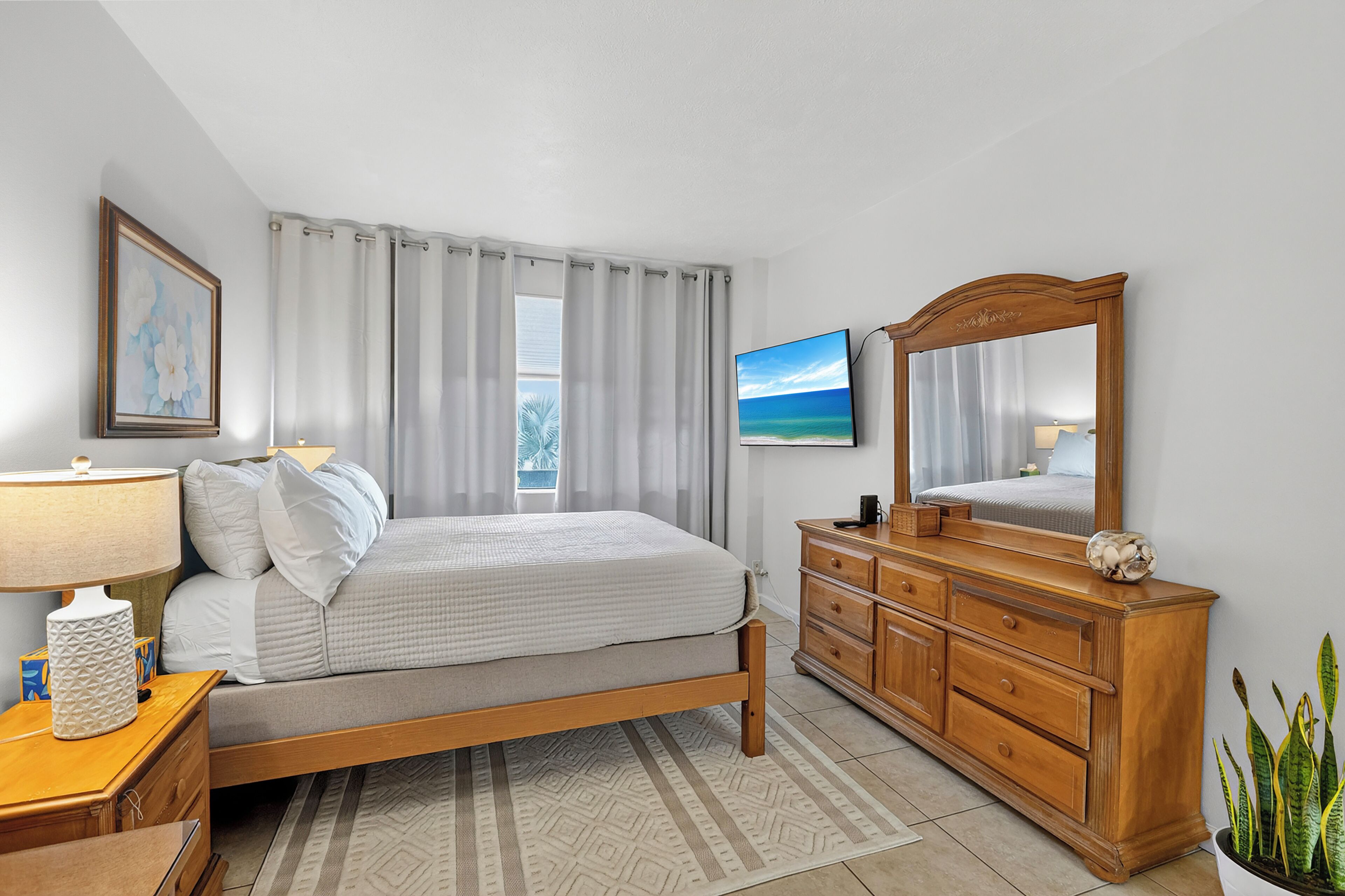 A bedroom with a bed, a dresser, a mirror, a lamp, a painting, and a potted plant.