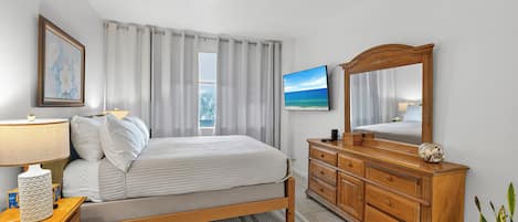 A bedroom with a bed, a dresser, a mirror, a lamp, a painting, and a potted plant.