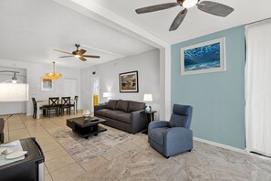 A living room with a ceiling fan, a dining area with a chandelier, and a painting on the wall. - 2BD Condo with Pool and Patio Ground Floor (Siesta Key)