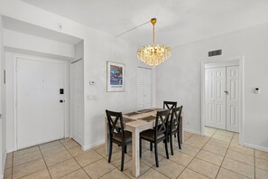 A dining area with a wooden table and chairs, a chandelier, and a door with a security camera. - 2BD Condo with Pool and Patio Ground Floor (Siesta Key)