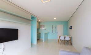 Una sala de estar moderna con televisor de pantalla plana, una zona de comedor con mesa y sillas, y una cocina con armarios y una ventana.
