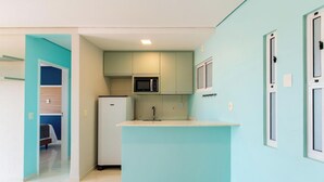 Uma cozinha compacta com geladeira, micro-ondas e um pequeno balcão central.